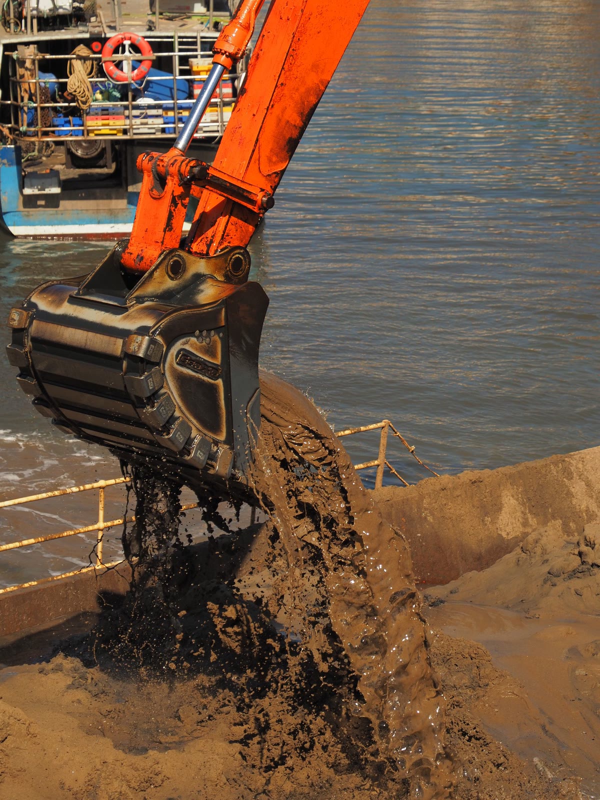 Excavator bucket lifting dredged sediment — dredging and reclamation