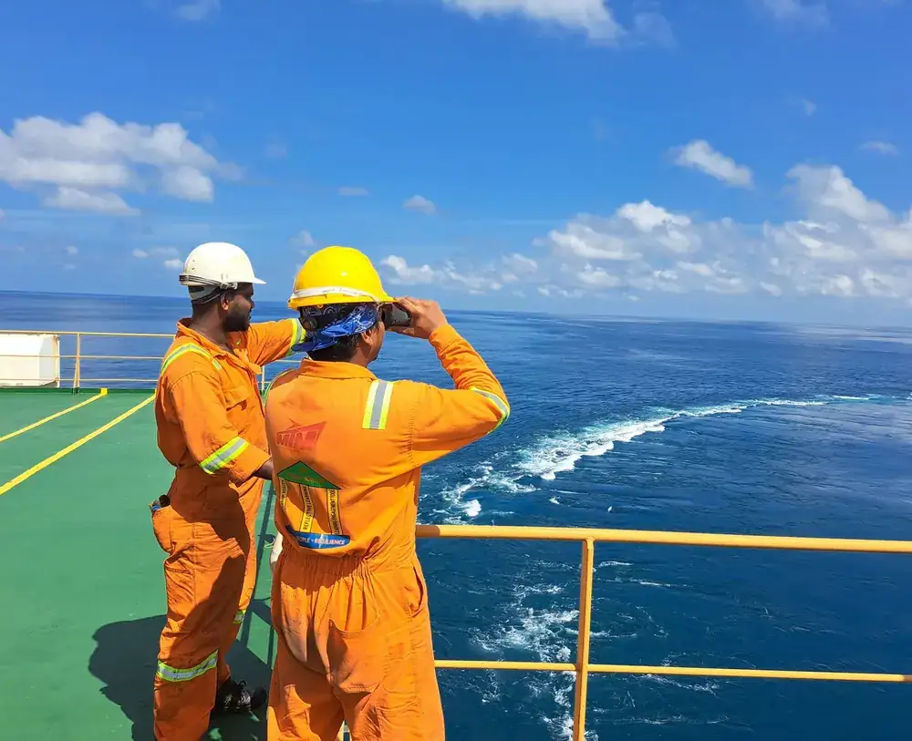 Two crew in orange coveralls and hard hats on a ship deck at sea