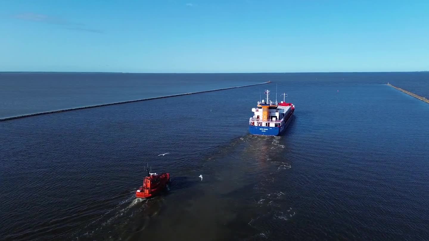 Tug escorting a cargo vessel out past a harbour breakwater